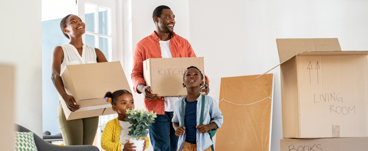A smiling family carrying moving boxes into their new home, representing attainable homeownership with Scott Credit Union home loans.