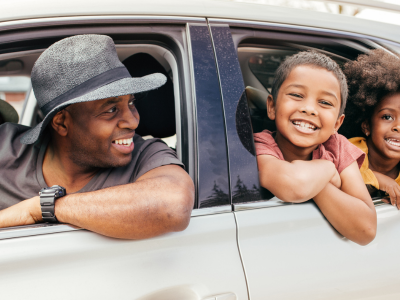 A happy family of four inside a modern silver vehicle looking out the open windows during a budget friendly regional summer road trip through Missouri and Illinois.