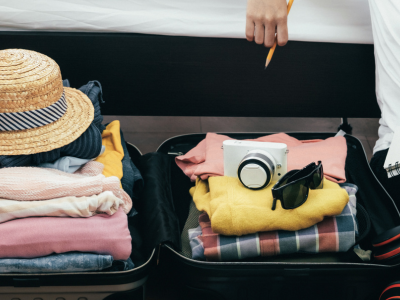 Person sitting next to an open suitcase with a notebook and pencil, budgeting after summer travel.