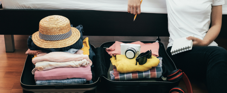 Person sitting next to an open suitcase with a notebook and pencil, budgeting after summer travel.