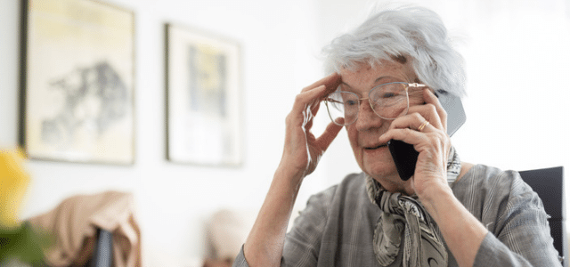 Concerned older woman holding her head while talking on a smartphone during an AI voice scam call.