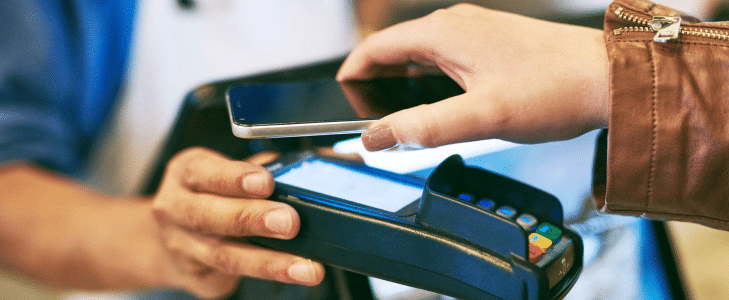 Customer holding a smartphone over a contactless payment terminal to complete a secure tap-to-pay transaction.